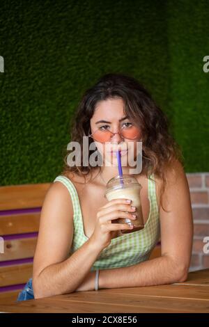 Jeune fille regardant l'appareil photo tout en buvant un smoothie. Banque D'Images