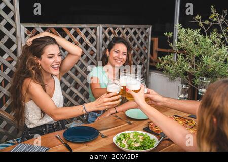 De beaux amis rient et applaudissent avec des bières et manger de la pizza. Groupe de personnes boire et manger concept Banque D'Images