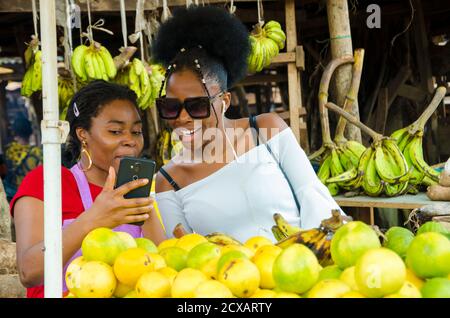 une belle femme du marché africain et sa cliente se sentent surpris sur ce qu'ils sur leur téléphone portable Banque D'Images