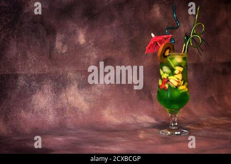 Un verre de jus à base de kiwi avec glace, morceaux de fruits, parapluie et pailles. Gros plan. Banque D'Images