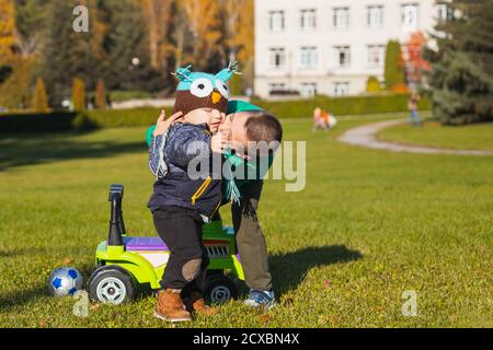 Deux gaies frères-garçons de différents âges ont le plaisir de jouer avec une grande jeep dans un fauteuil roulant sur un terrain vert lors d'une chaude journée d'été. Frères amicaux Banque D'Images