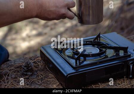 Tisane dans une tasse en métal à la main sur un poêle à gaz portable. La main d'un homme contient du thé à base de plantes fait de hanches roses et de diverses herbes dans un acier inoxydable Banque D'Images