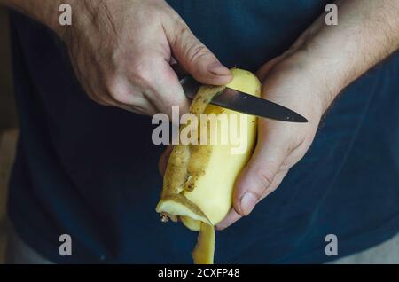 Un homme mûr épluche des pommes de terre crues avec un couteau de cuisine. Gros plan des mains d'un homme du Caucase. Processus de préparation des aliments. 44 ans. Sélectif f Banque D'Images