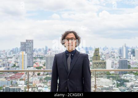 Homme d'affaires japonais avec des cheveux bouclés portant des lunettes contre vue de la ville Banque D'Images