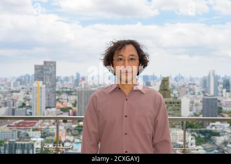 Homme d'affaires japonais avec des cheveux bouclés portant des lunettes contre vue de la ville Banque D'Images