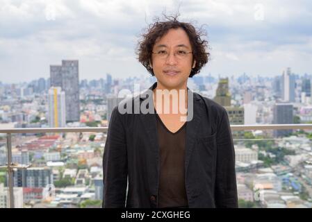 Homme d'affaires japonais aux cheveux bouclés portant un costume contre la vue de la ville Banque D'Images