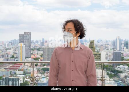 Portrait de l'homme d'affaires japonais pensant avec masque contre vue de la ville Banque D'Images