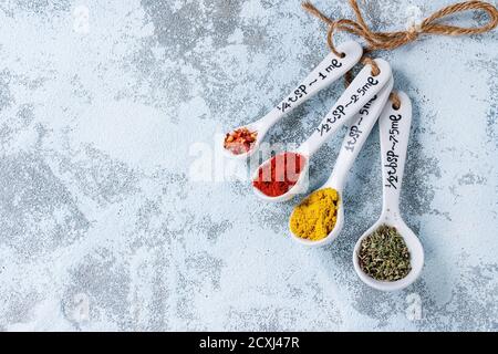 Assortiment d'épices moulues colorées en blanc différentes cuillères à mesurer en céramique sur fond blanc texturé. Avec espace de copie. Vue de dessus Banque D'Images