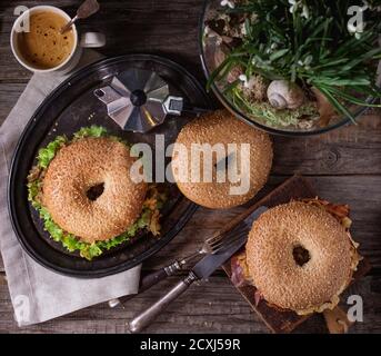 Deux Bagels avec stew boeuf, salade fraîche, bacon, œufs brouillés et oignon frit servi sur le plateau métallique vintage avec bouquet de perce-neige, une tasse de café Banque D'Images