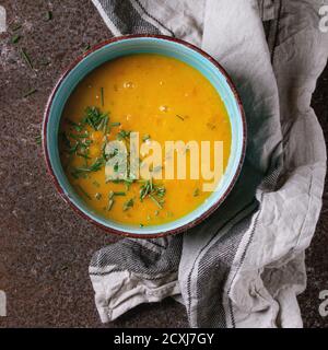 Bol en céramique bleue de soupe de carottes, servi avec de la ciboulette d'oignon et une serviette de cuisine sur fond de fer rouillé. Style rustique sombre, vue sur le dessus Banque D'Images