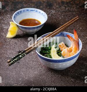 Bols chinois avec épinards cuits et crevettes frites crevettes crevettes aux graines de citron et de sésame, sauce soja et baguettes sur fond de fer ancien. Style asiatique Banque D'Images