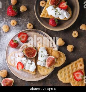 Galettes en forme de coeur avec framboises jaunes, fraises, figues en tranches, fromage ricotta et poudre de sucre sur des assiettes en céramique sur fond de bois foncé Banque D'Images