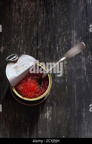 Ouvrir boîte de caviar rouge et cuillère en argent sur la surface en bois. Style rustique foncé. Vue d'en haut. Banque D'Images