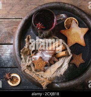 Tasse en verre d'épices à vin chaud rouge chaud, biscuits sablés au sucre en forme d'étoile, poudre d'anis et de cannelle dans un plateau en argile sur fond de bois sombre. CHRI Banque D'Images