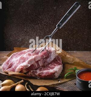 Viande de bœuf crue cou de porc sur la planche à découper avec l'oignon d'échalote, la marinade à la tomate, le basilic et l'assaisonnement, servi avec une fourchette à viande sur le vieux dos en bois Banque D'Images