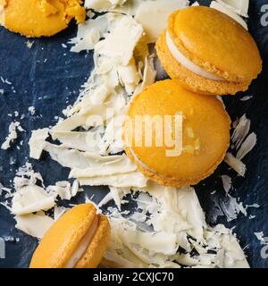 Macarons faits maison au citron orange entier et cassé avec du blanc haché chocolat, sucre d'agrumes et zeste sur une planche en verre foncé au-dessus du fond de texture noir Banque D'Images