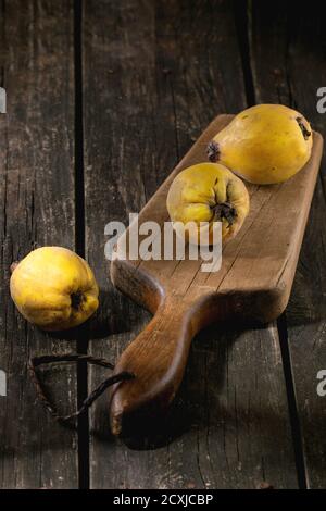 Ensemble de trois coings juteux sur la vieille planche à hacher sur table en bois dans la lumière du soleil. Style rustique foncé. Banque D'Images