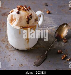 Tasse en céramique vintage avec crème glacée au caramel et au beurre de noisette maison, servie avec du sirop de caramel et des noix croustillantes sur du backgroun texturé en métal rouillé Banque D'Images