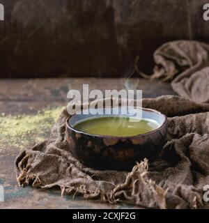Tasse en céramique de thé vert matcha sur un chiffon en toile de sackCloth humide sur fond texturé en bois sombre. Une alimentation saine. Avec espace de copie. Image carrée Banque D'Images