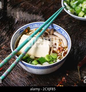 Bol en porcelaine chinoise de soupe asiatique de ramen avec feta, nouilles, oignons de printemps et champignons, servi avec des baguettes turquoise sur une ancienne patte en bois Banque D'Images