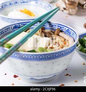 Bol en porcelaine chinoise de soupe asiatique de ramen avec feta, nouilles, oignons de printemps et champignons, servi avec des baguettes turquoise et coupé en tranches Banque D'Images