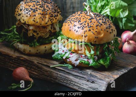 Deux hamburgers de légumes faits maison avec patate douce, radis frais et pousses de pois, servis sur une planche à découper en bois sur fond de bois. Style rustique sombre Banque D'Images