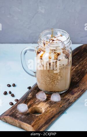 Pot mason de verre avec de la glace café avec crème fouettée, crème glacée et sauce au chocolat, servi avec des grains de café et des cubes de glace sur la planche à découper en bois ove Banque D'Images
