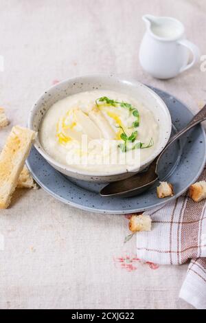 Bol de soupe crème d'asperges blanches avec des pousses de pois et de grillé, servi avec verseuse de lait sur nappe gris Banque D'Images