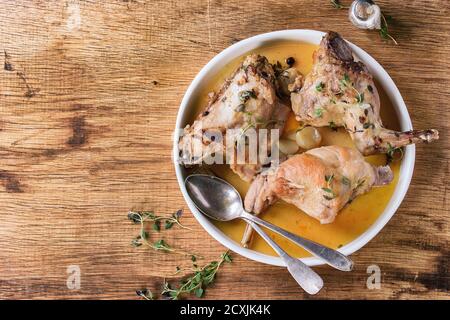 Assiette en céramique blanche avec un lapin cuit au bouillon, au sel et aux herbes, servie avec des couverts vintage sur fond de bois. Plan de travail avec espace de copie Banque D'Images