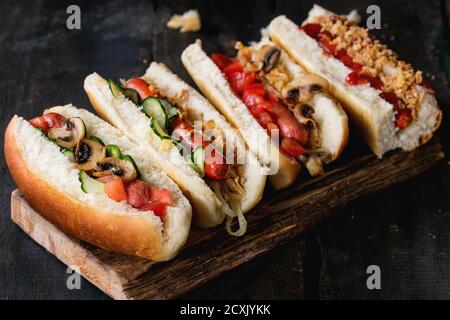 Assortiment de hot dogs faits maison avec saucisse, oignon frit, tomates et concombres, servis sur planche à découper en bois sur fond de bois ancien. Rustiques Banque D'Images