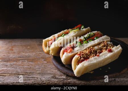 Assortiment de hot dogs faits maison avec saucisse, oignon frit, tomates et concombres, servis sur planche à découper en bois sur fond de bois ancien. Russe foncé Banque D'Images