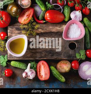 Le fond de la nourriture avec des tomates, des concombres, des herbes, de l'huile d'olive et du sel. Salade de légumes thème de saison avec planche à découper en bois et espace pour le texte. Il Banque D'Images