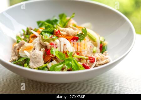 Cuisine thaïlandaise, salade épicée de nouilles décuites ou Yum Woon Sen en langue thaïlandaise. Gros plan des aliments dans un bol blanc sur une table, lumière naturelle. Banque D'Images