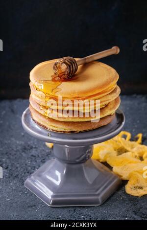 Pile de crêpes à la curcuma américaines maison jaune ombré au miel sauce servie sur un support à gâteau avec un balancier en bois sur du noir fond de texture de pierre Banque D'Images