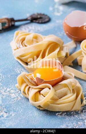 Matières premières fraîches maison pâtes non cuites torsadée tagliatelle aux jaunes d'oeufs, Shell et les pâtes cutter bleu clair sur fond de béton. Banque D'Images