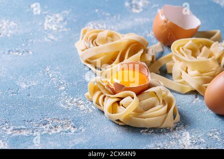 Matières premières fraîches maison pâtes non cuites torsadée tagliatelle aux jaunes d'oeufs, Shell et les pâtes cutter bleu clair sur fond de béton. Banque D'Images