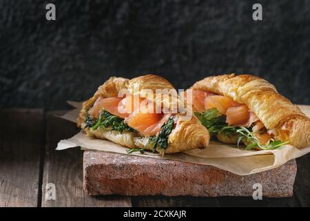 Deux croissants avec du saumon salé, fumé et à la roquette épinard servi sur du papier sulfurisé conseil terre cuite ancienne en bois foncé sur arrière-plan. Copy space Banque D'Images