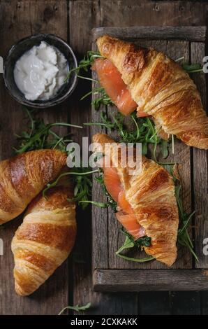 Un croissant avec du saumon salé, fumé et épinards servi avec roquette bol de fromage à la crème sur la vieille table en bois sombre. Vue d'en haut Banque D'Images