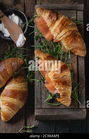 Un croissant avec du saumon salé, fumé et épinards servi avec roquette bol de fromage à la crème sur la vieille table en bois sombre. Vue d'en haut Banque D'Images