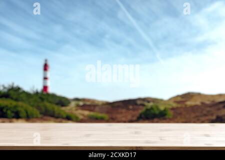 Barre en bois vide sur le fond et vue floue sur le paysage de bord de mer avec un phare rayé rouge-blanc. Journée ensoleillée d'été sur la côte de la mer. Banque D'Images