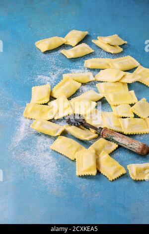 Maked frais crus crus ravioli pâtes italiennes avec la farine et les pâtes vintage bleu vif sur la faucheuse arrière-plan en bois. Vue de dessus avec l'exemplaire de l'espace. Banque D'Images