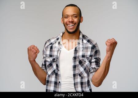 Un jeune homme afro-américain gagne oui en faisant des gestes sur fond gris clair Banque D'Images