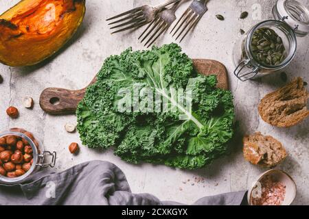 Vue de dessus de kale frais sur une planche à découper en bois entourée de produits saisonniers d'automne.citrouille rôtie, pain, noix et graines. Banque D'Images