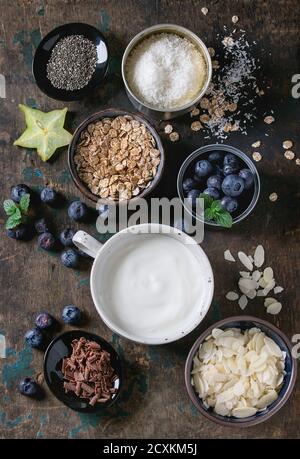 Ingrédients pour faire des smoothie déjeuner sain. Bols de yaourt, bleuets, granola, noix de coco, graines de chia amande, lait, chocolat, menthe, caram Banque D'Images