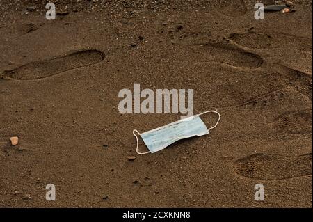 Déchets pendant COVID-19 avec du sable en arrière-plan. Jeté dans des masques faciaux à usage unique du coronavirus océanique. Pollution plastique environnementale et côtière. Banque D'Images