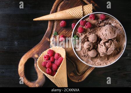 Bol de glace au chocolat fait maison avec les framboises, menthe et cornet gaufré sur bois servant au fond de bois brûlé noir. Vue supérieure w Banque D'Images