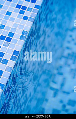 Taches d'eau d'une goutte aux marches avec une mosaïque bleue dans la piscine. Banque D'Images