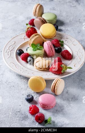 Variété de macarons français doux et colorés au dessert avec différents macarons garnitures servies sur plaque vintage blanche avec fleurs de printemps et baies Banque D'Images