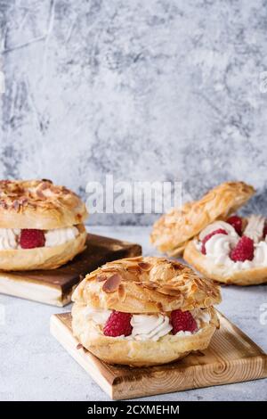 Gâteau de chax maison Paris Brest aux framboises, aux amandes et au romarin, servi sur un plateau de service en bois sur fond de texture bleu gris. Français Banque D'Images