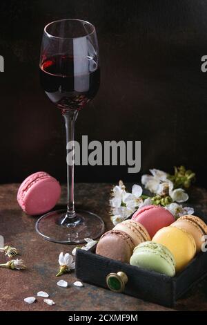 Verre de Porto avec variété de doux français coloré dessert macarons macarons avec différentes garnitures servies avec des fleurs printanières sur texture sombre Banque D'Images
